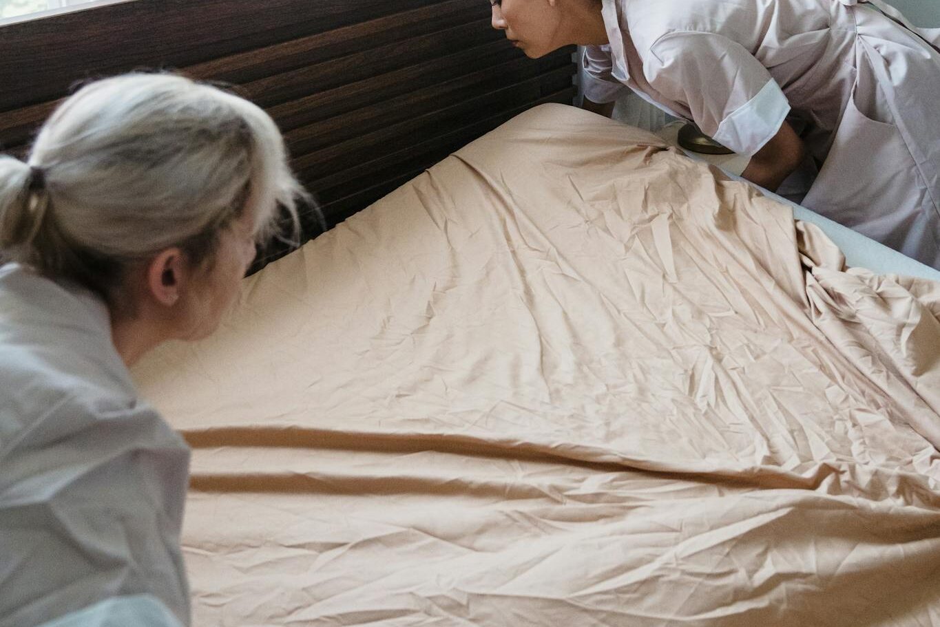 Hotel maids changing bed linens, showcasing professional housekeeping in a bright room.