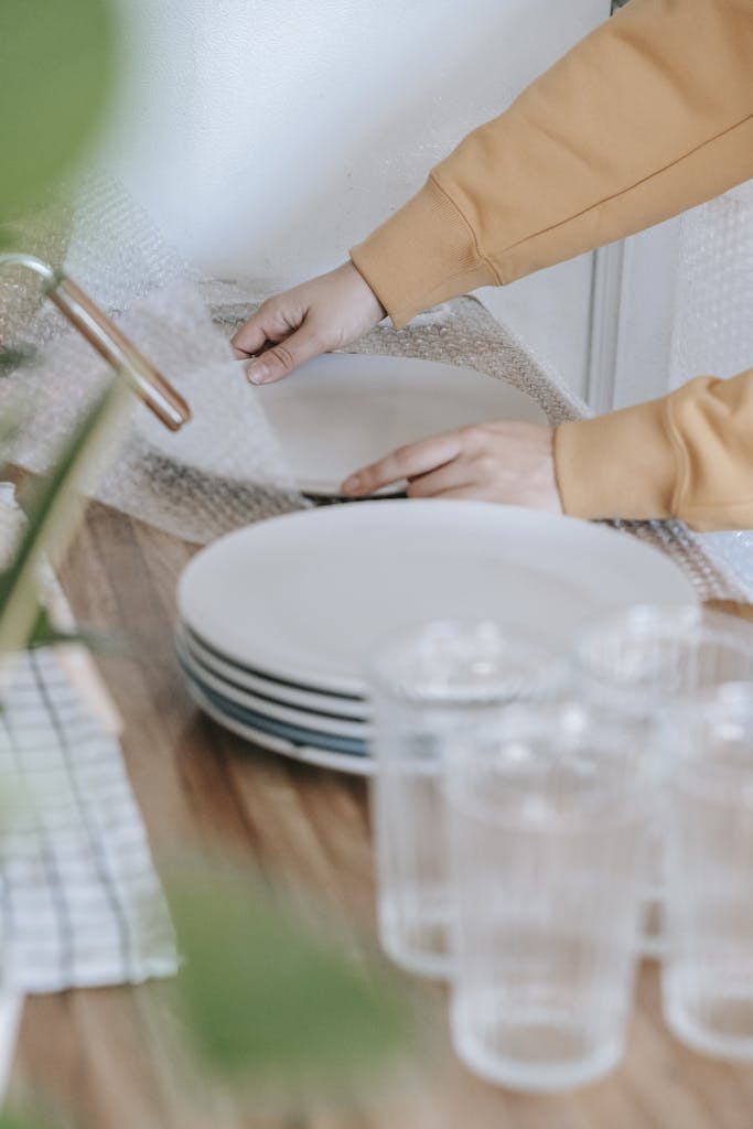 Woman packing white plates in bubble wrap on kitchen counter.